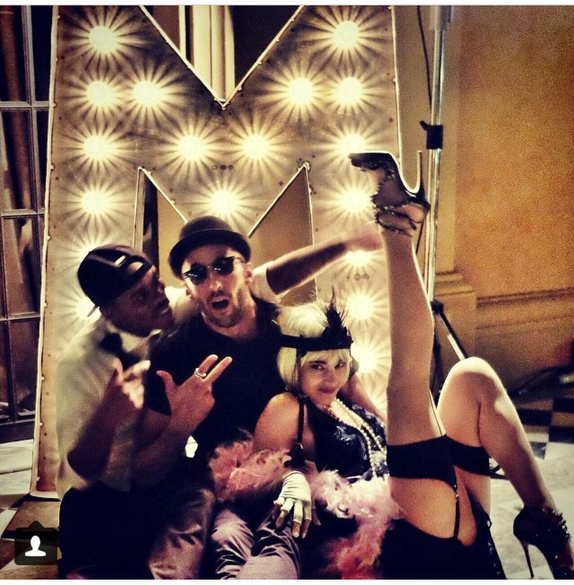 Dancers posing in front of a giant lit marquee M
