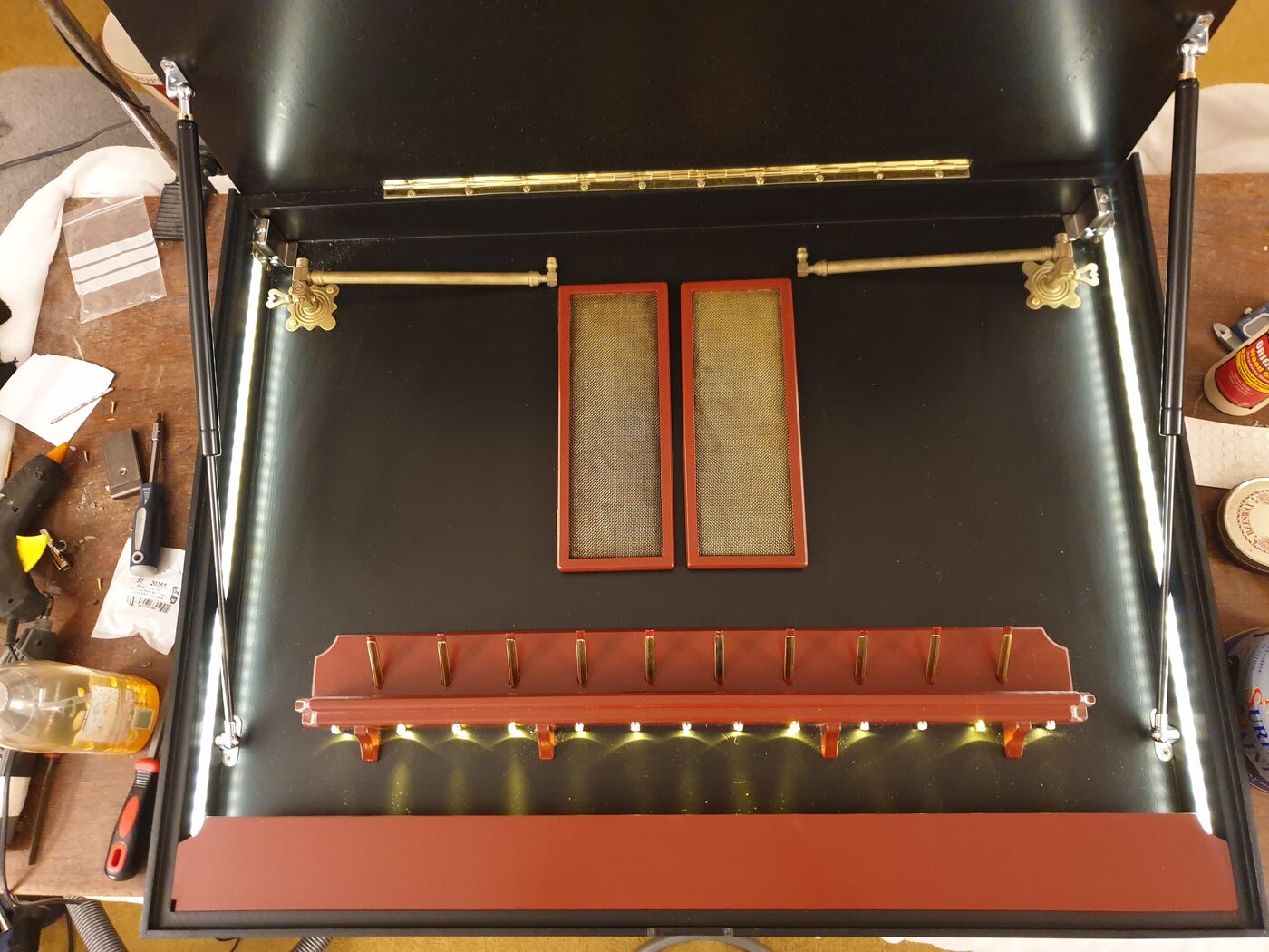 Open wall jewellery cabinet with lit interior, brass rails and red trays