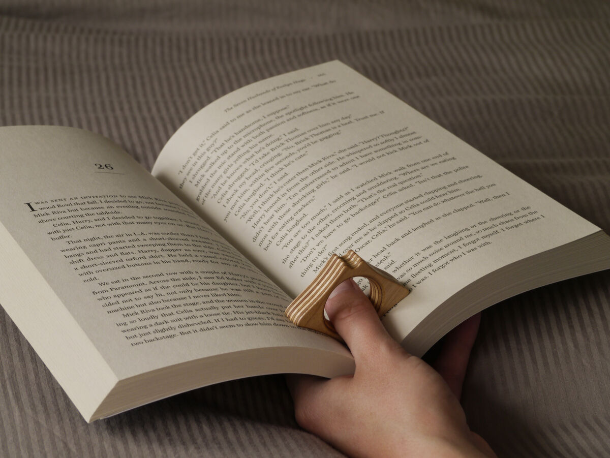 Wooden PageRay page holder on a thumb, holding a paperback open